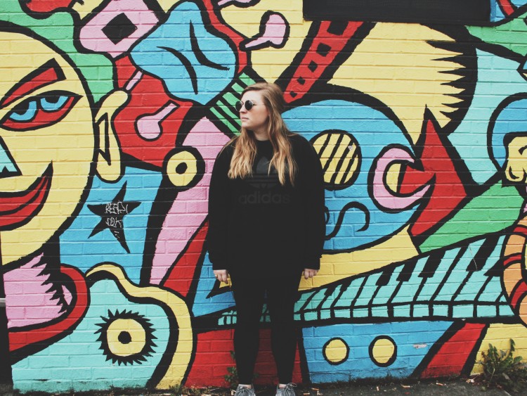 Woman with long blonde hair standing in front of a colorful mural.