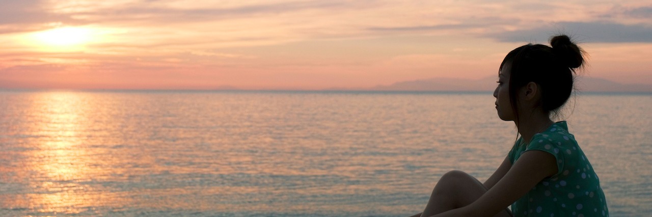 7 Lessons To Recover Your Spirit After A Life Crisis woman sitting looking and sunset over ocean