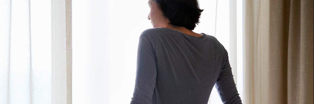 Crohn's Disease, the Spoon Theory and Making Decisions About the Day Woman looking through window, sitting on bed, back view