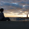 A girl sitting and looking at the light house early in the morning.