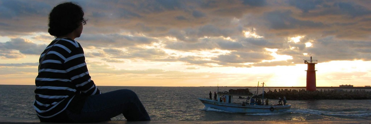 A girl sitting and looking at the light house early in the morning.