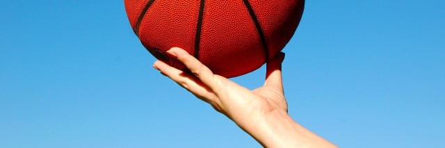 basketball being held in hand against a brilliant blue sky
