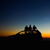 three friends sitting on their car at sunset
