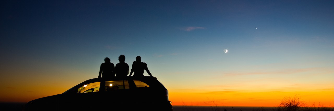 three friends sitting on their car at sunset