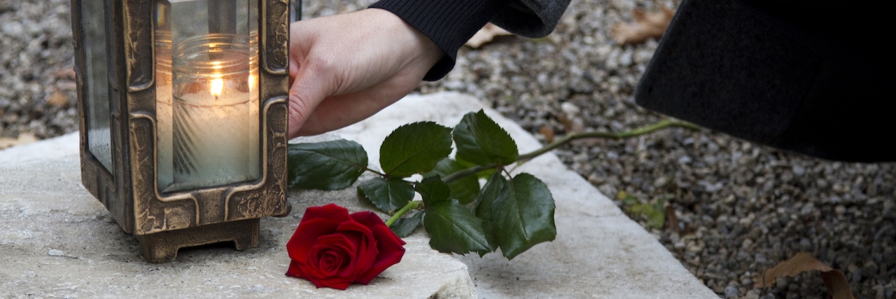 Why We Should Stop Apologizing for Those Who Died by Suicide Woman lighting a candle next to a rose