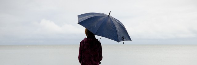 A person sitting on a dock, holding an umbrella on an overcast day