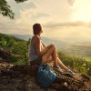 Girl sits on the edge of cliff and looking at sun valley and mountains