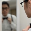 A man straightening his bow tie while looking at his reflection.