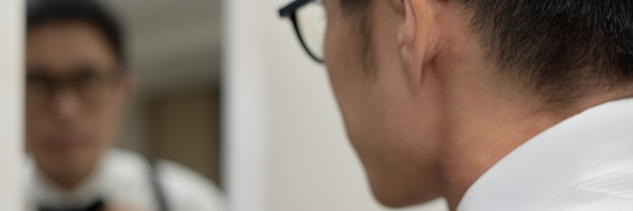 How to Survive and Thrive With Body Dysmorphic Disorder A man straightening his bow tie while looking at his reflection.