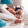 Woman in bed reaching for her mobile phone on nightstand