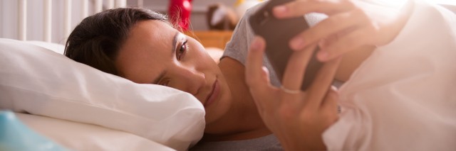 Woman Lying In Bed Checking Messages On Mobile Phone