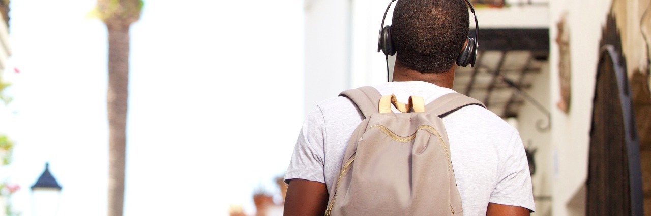 Rear view of man with backpack wearing headphones and walking