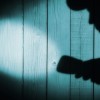 Unrecognizable burglar with flashlight in shadow on wood background, with space for text or image