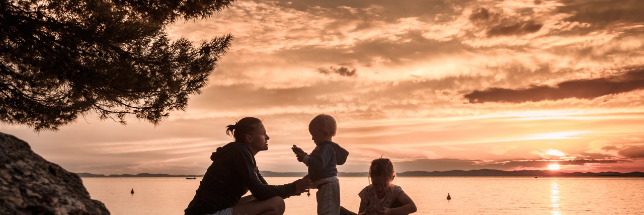 silhouette of mother playing with children on a beach at sunset