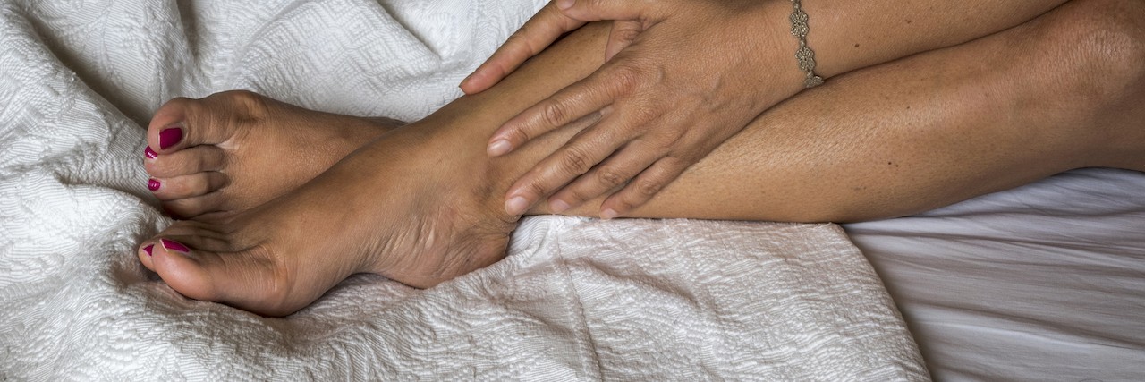 Symptoms of Diabetic Neuropathy Pain The woman massaging her legs on a bed, bed with embroidered sheets, white background, side view