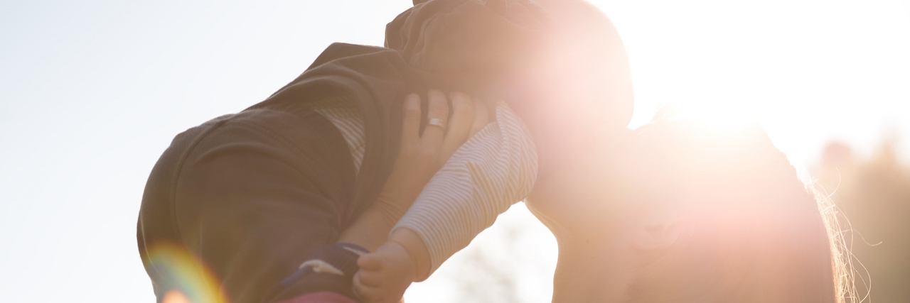 What to Say to Sick Child Instead of 'It's Going to Be All Right' Woman Lifting and Kissing Baby Backlit by Bright Sunlight Outdoors