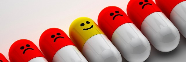 pills lined up with frowney faces on them. One has a happy face.
