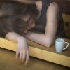 Young woman lying on her arms on the table in cafe in front of laptop with cup of coffee, sleepy, tired, overworked