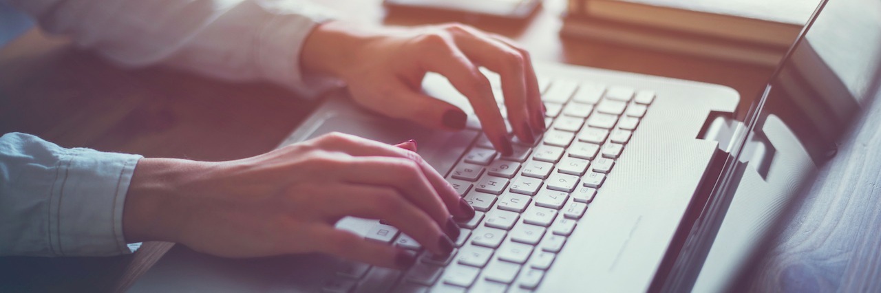 'What Is the Life Expectancy for Someone With POTS?' Working at home with laptop woman writing a blog. Female hands on the keyboard.