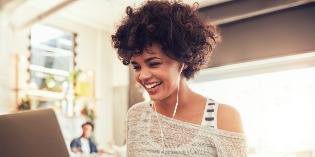 Image of happy woman using laptop while sitting at cafe. Young african american woman sitting in a coffee shop and working on laptop.