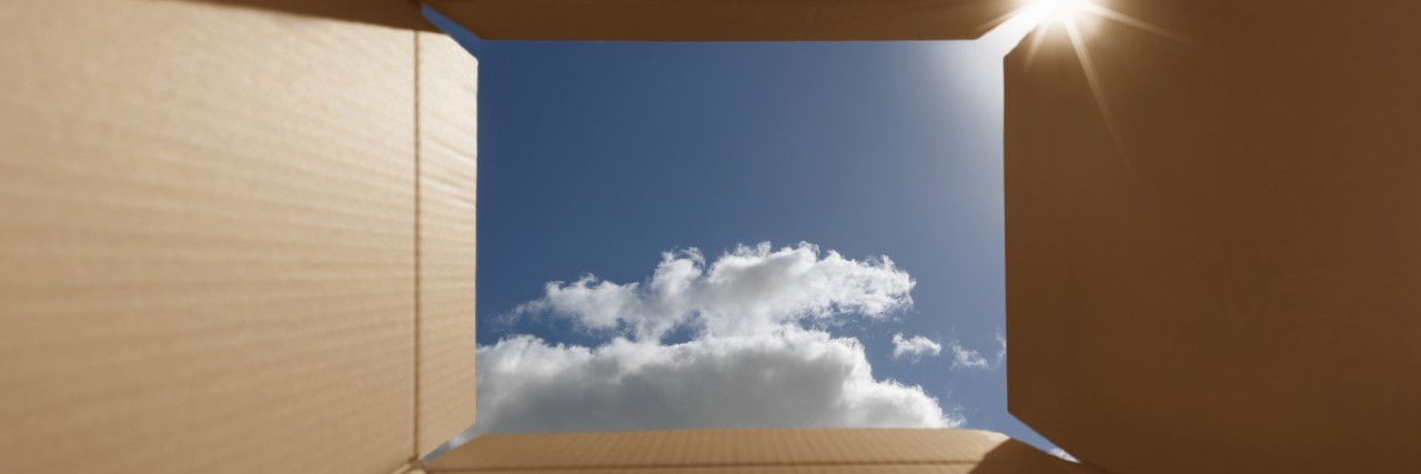 Autism Spectrum Disorder and 'Thinking Outside the Box' Conceptual shot illustrating the phrase 'thinking outside the box'. Implies inspirational thoughts, bright new ideas, imagination and escaping from the norm. The box has areas for copy space. Carefully positioned to show the bright blue sky and also lens flare from the sun.