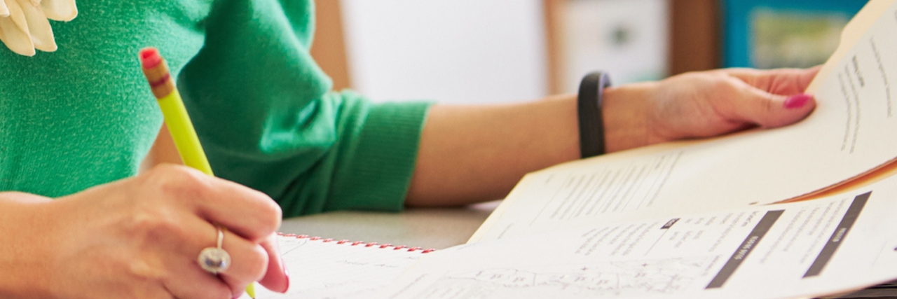 Telling My Son's Teachers About His IBD Before School Starts Teacher wearing a green cardigan, sitting a desk with paperwork