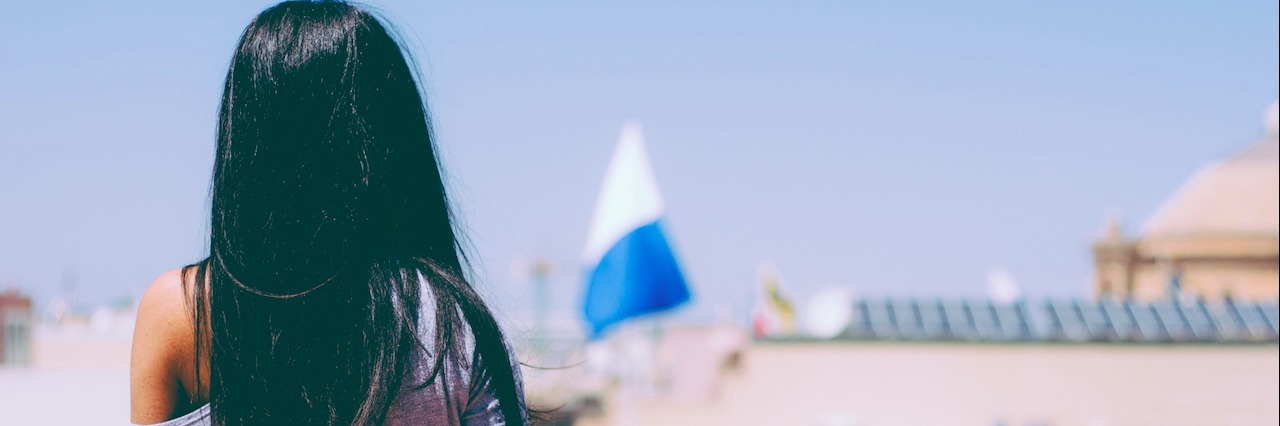 When I Realized My Pain From Fibromyalgia Was Here to Stay Young girl with a long streight black hair looking at the view from the balcony