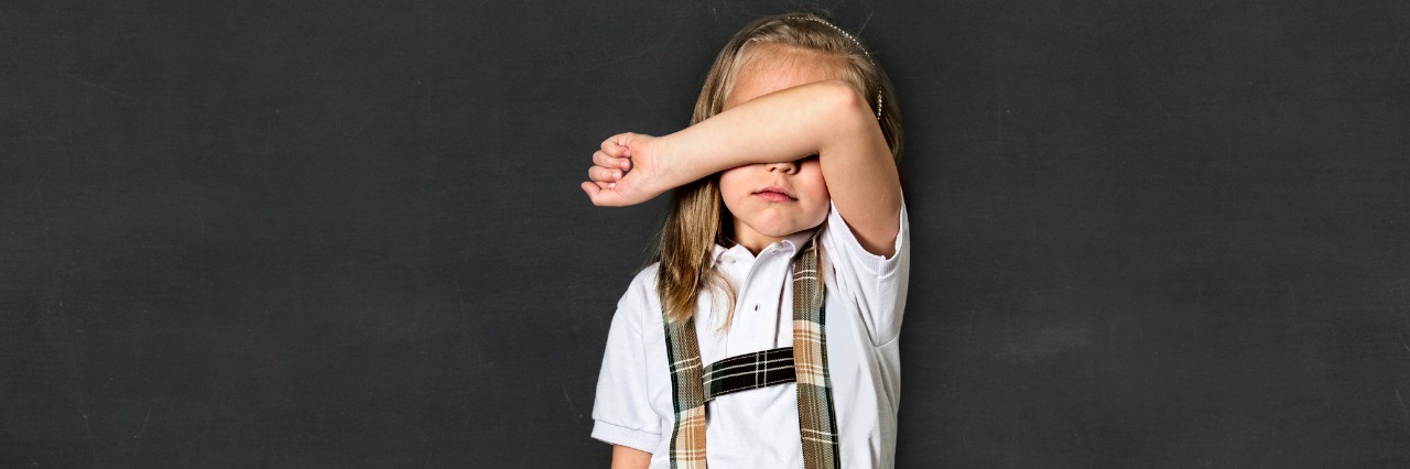 First Day of School for the Mom of a Child With a Mental Illness young sweet junior schoolgirl with blonde hair crying sad and shy standing isolated in front of blackboard holding chalk in her little hand wearing school uniform in children education stress