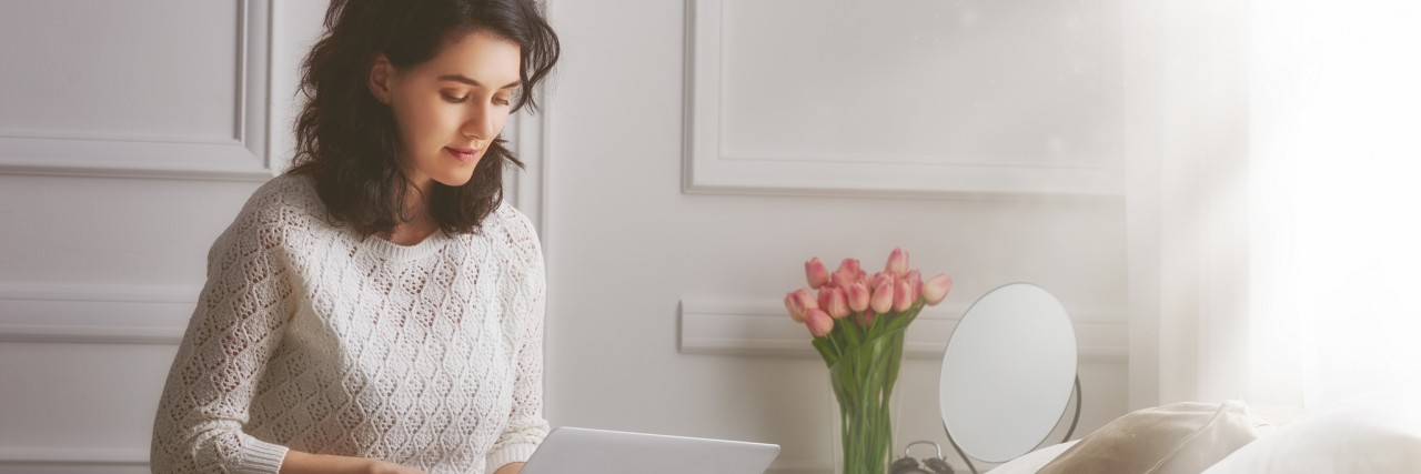 Living a Dream Life With a Progressive Neurological Disorder happy woman sitting in bed and writing on laptop