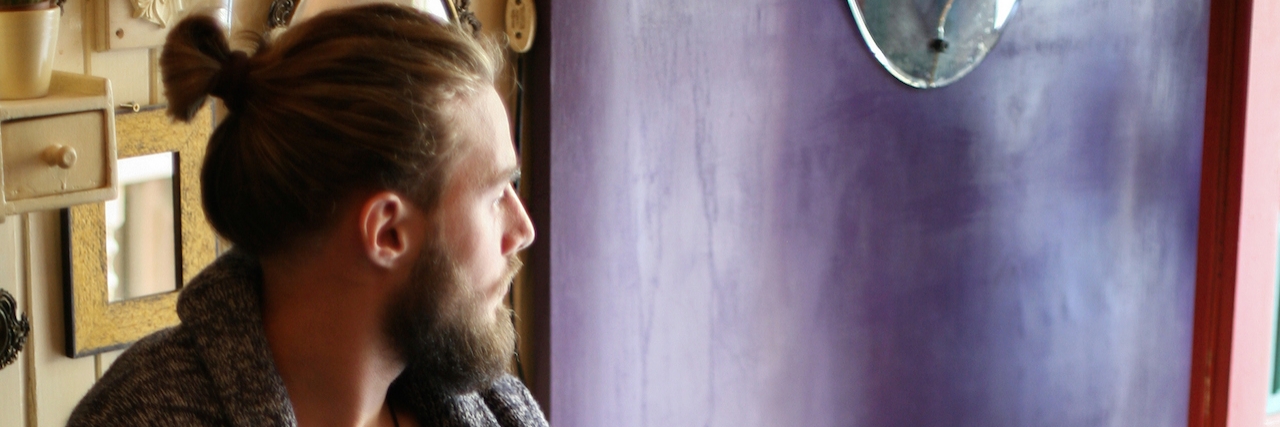 A man with a beard sitting in a cafe, looking outside
