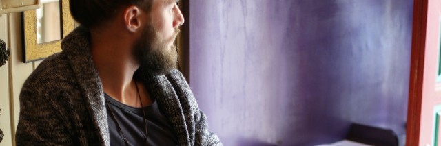 A man with a beard sitting in a cafe, looking outside