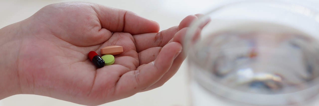 woman hands holding pills and water glass, taking medicine pills