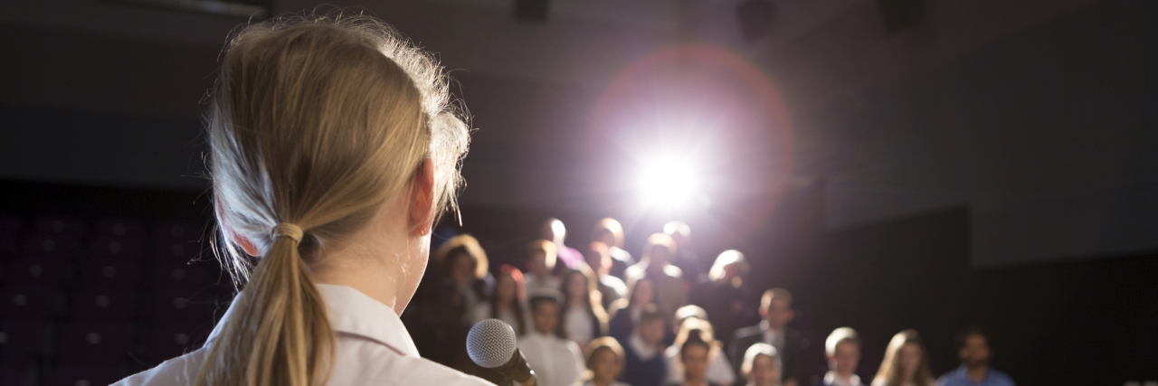 My Plan to Survive High School With Hypotonia Female student making a speech. She is standing at a podium and smiling to the crowd.