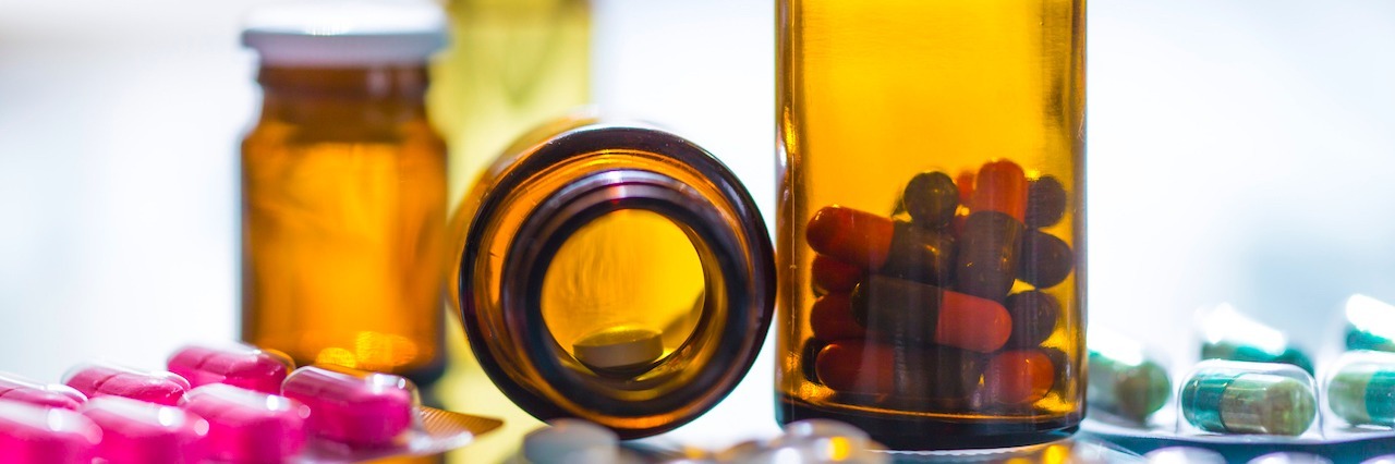 Why I Don't Judge Alternative Pain Relief Treatments Anymore medicines in blister packaging and brown glasses in backlight