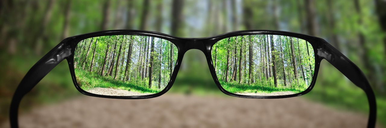 When Depression Makes You Think the Worst of Everyone glasses being held up in front of a forest