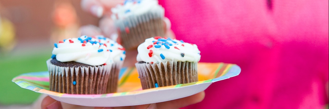 What It Feels Like to Eat Gluten If You Have Celiac Disease Hand holding plate of cupcakes outdoors