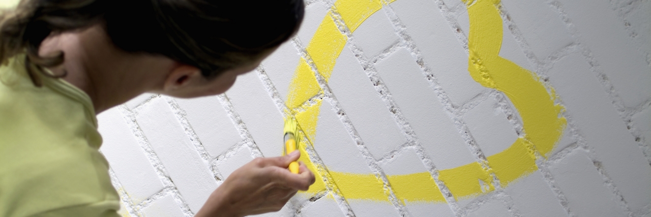 Anxiety: Everyday Ways to Promote Good Mental Health Rear view of a woman painting a yellow heart on a brick wall