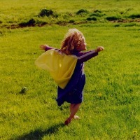 little girl running with arms up across grass field