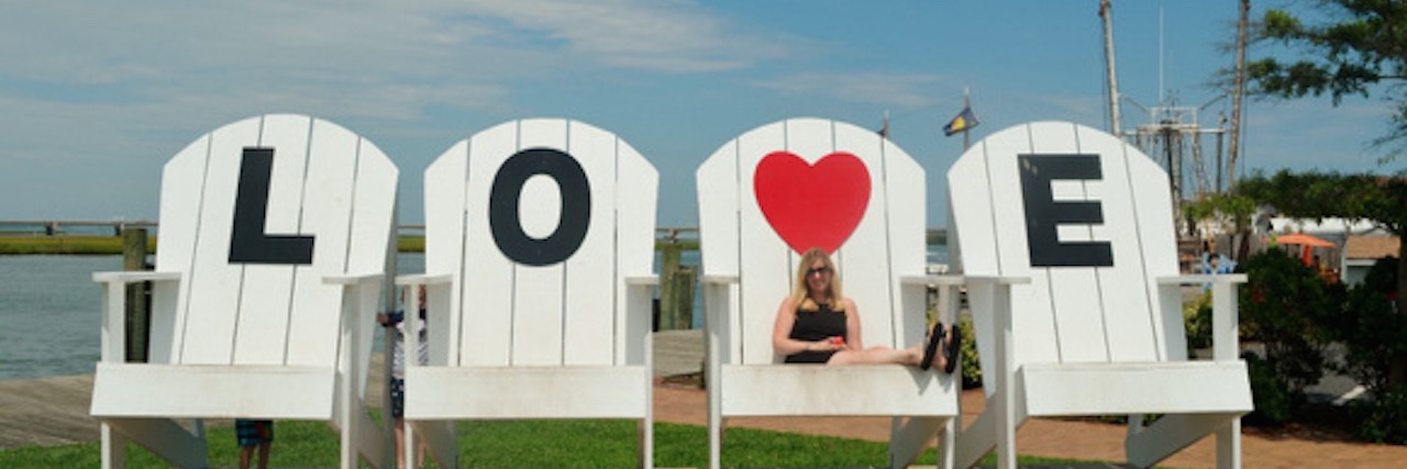 Woman sitting on large white chairs that spell out LOVE
