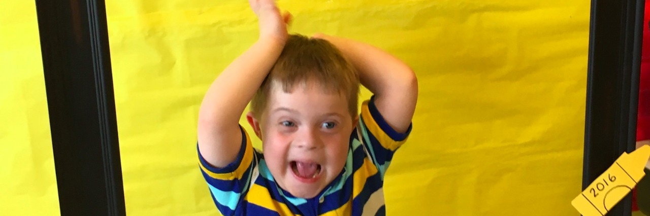 A Letter to My Son With Down Syndrome as He Starts Kindergarten The author's son standing behind a frame that says "My 1st Day of Kindergarten"