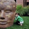 woman crouching on ground whispering in ear of head statue