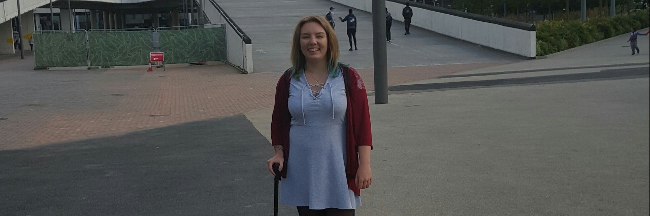 Why I Started Using a Cane for My Fibromyalgia woman standing outside arena with a cane