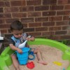 Boy sitting in a sand pit playing with a spoon and bucket.