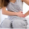 woman holding stomach sitting on bed