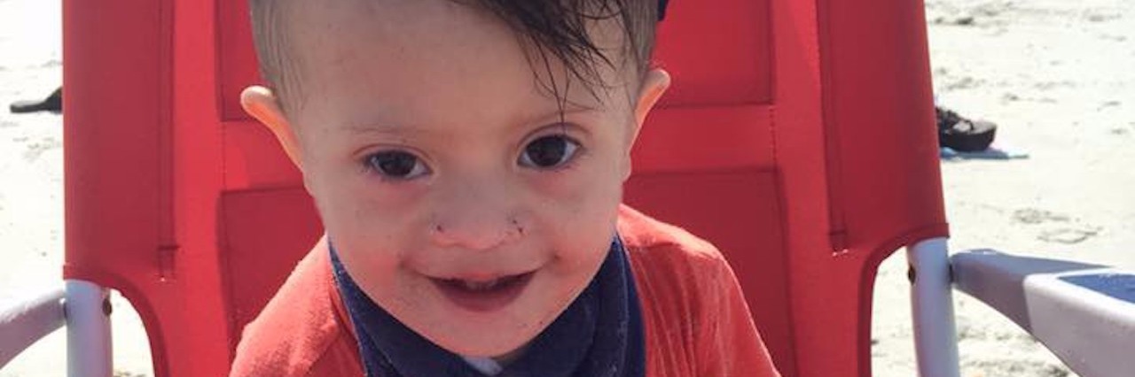Deciding to Keep Our Baby With Down Syndrome After the Panorama little boy with down syndrome sitting in a chair on the beach