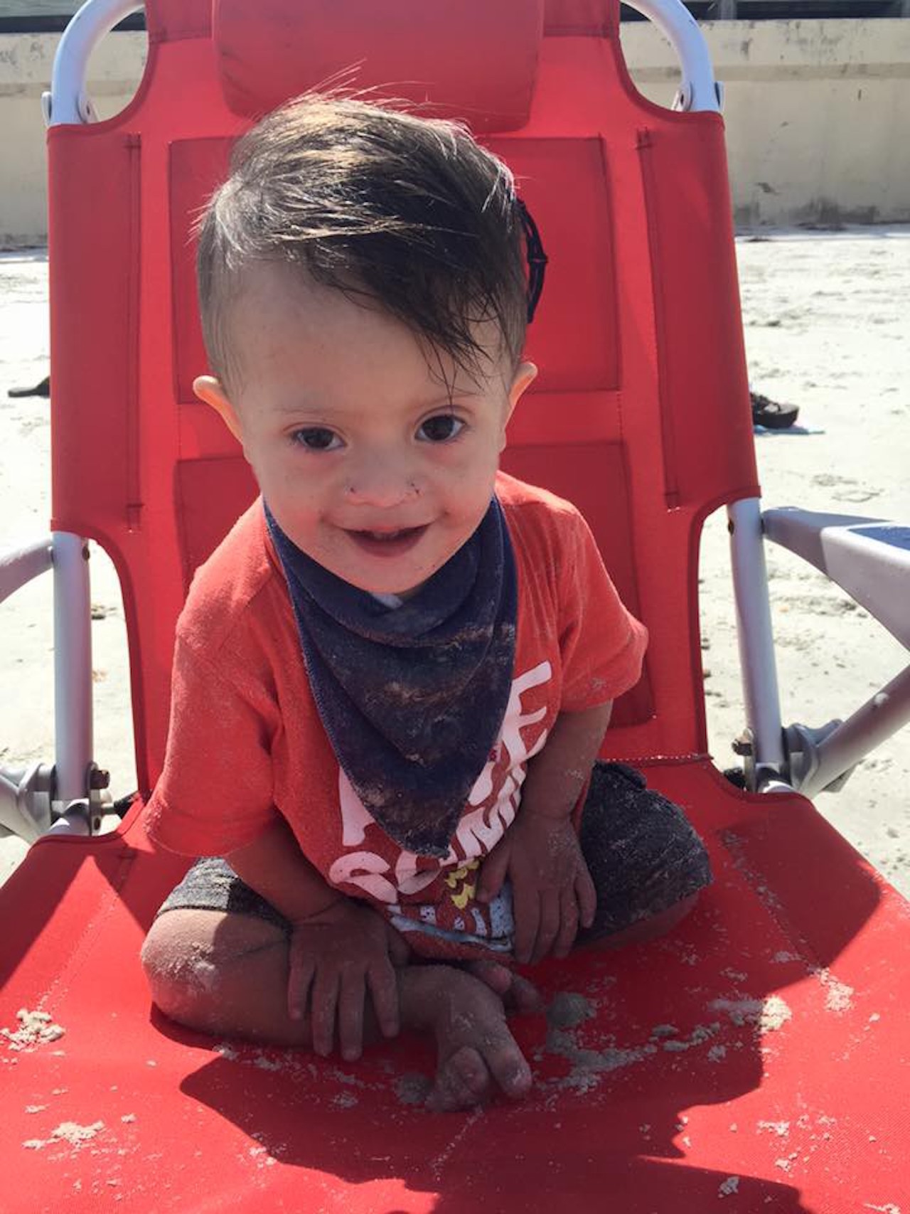 little boy with down syndrome sitting in a chair on the beach