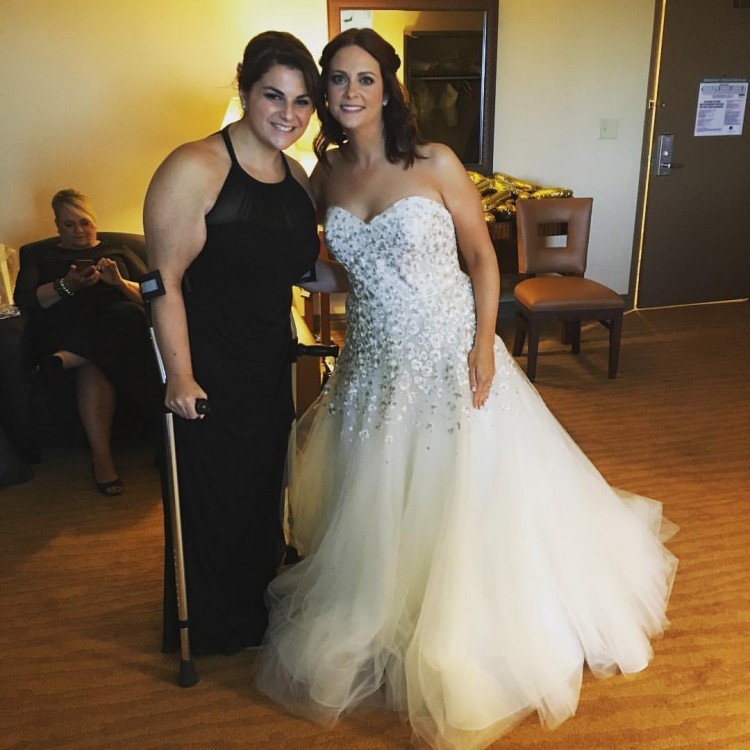 bride in wedding dress next to woman standing with crutch