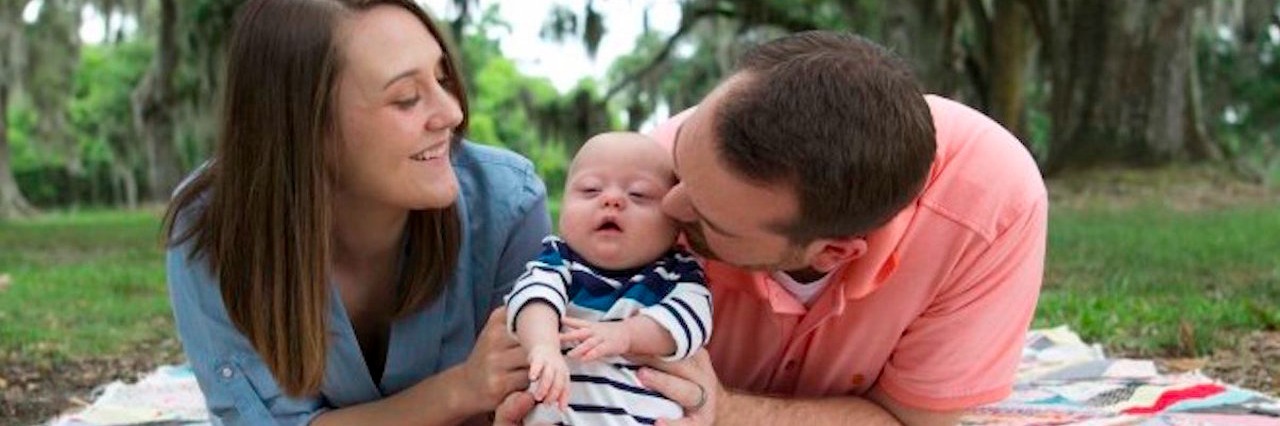 Down Syndrome: Father Explains Importance of Raising Awareness mom and dad with baby lying on a blanket outside