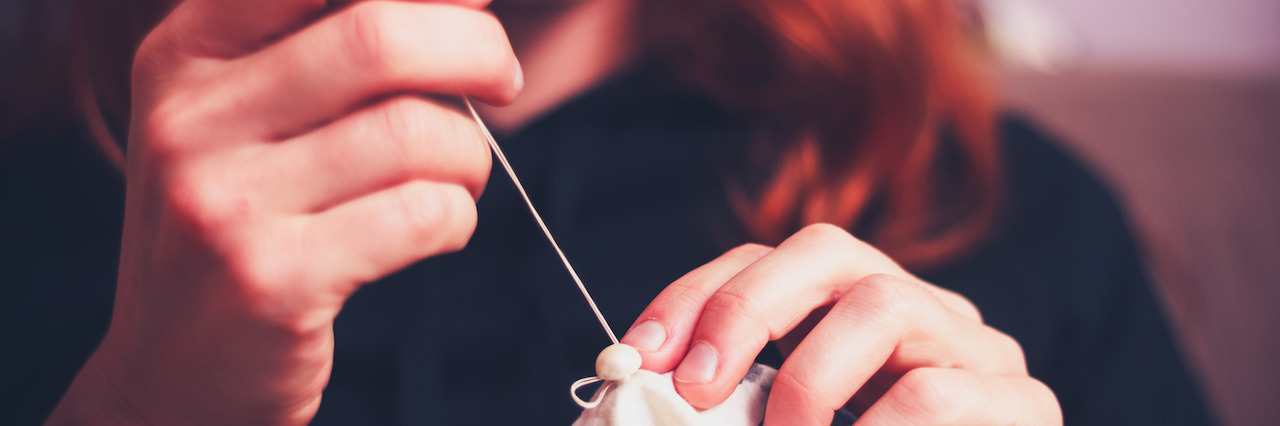 The Shame in Talking About Mental Illness Vs. Chronic Illness Close up on a young woman's hands as she is sewing