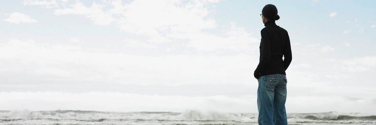 Chronic Illness: My Body Became My Own Worst Enemy woman standing on rocky beach